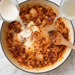 Cream and pasta water added to kimchi in the same ivory skillet