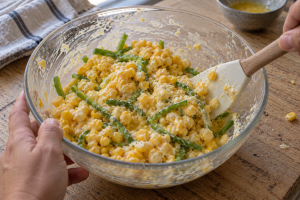 Sweet corn mixture folded with thin green bell pepper strips in a used glass bowl