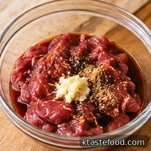 Raw thin-sliced beef in a glass bowl with soy marinade and minced garlic, before cooking.