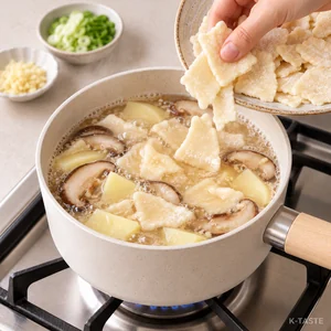 Adding store-bought potato sujebi pieces to the simmering mushroom and potato broth